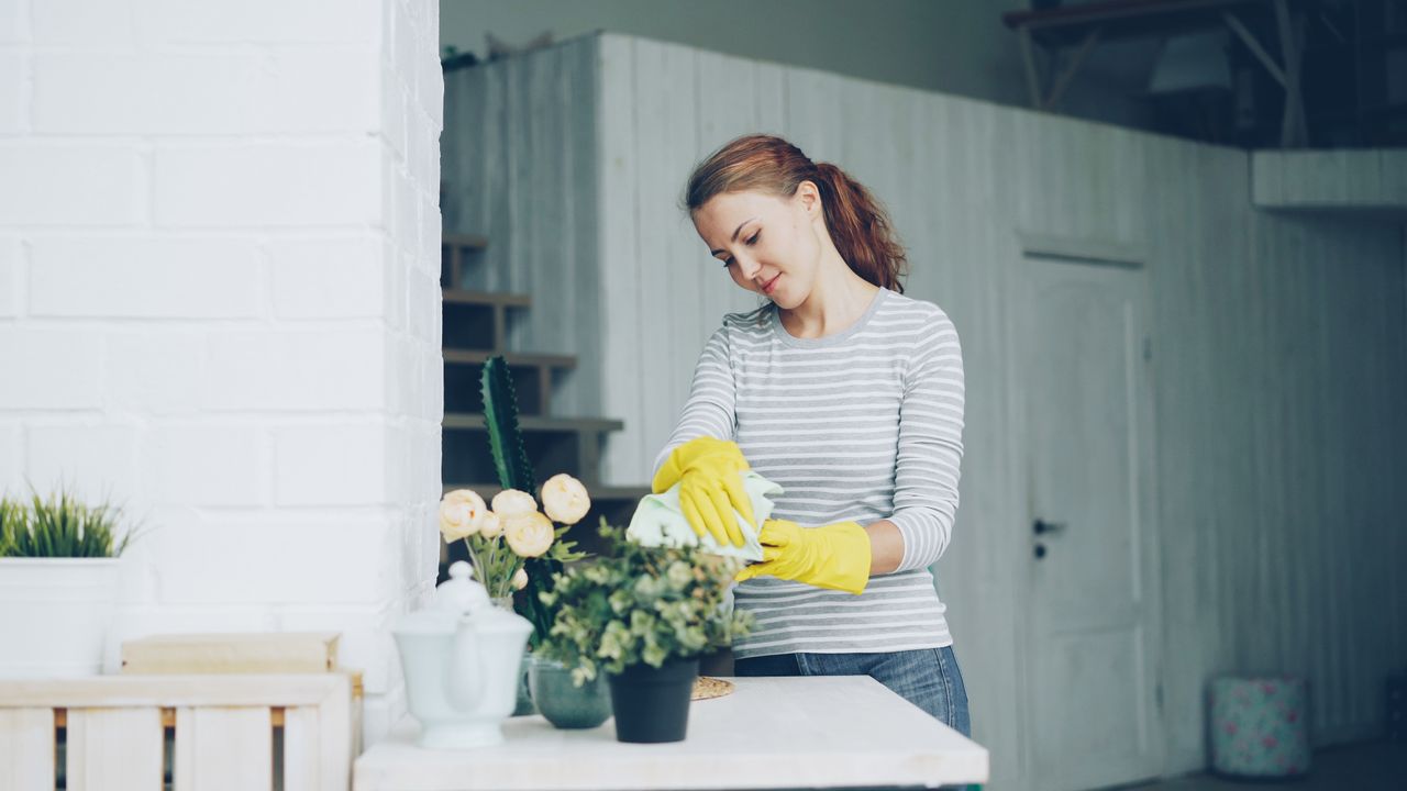 The Art of Drawing Readers In: Your attractive post title goes here Young woman cleaning home with yellow gloves and striped shirt, focused on tidying indoors.